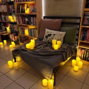 Bett und Bücherregale mit entzündeten Kerzen, die eine romantische Stimmung für ein Date in einer Buchhandlung in Mülheim an der Ruhr kreieren. Eine kuschelige Decke und Kissen schaffen eine gemütliche Atmosphäre für ein besonderes Date.
