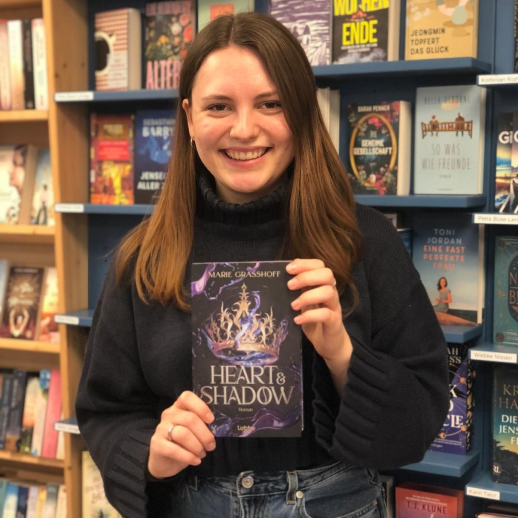 Unsere Buchhändlerin hält das Buch "Heart & Shadow" von Marie Graßhoff in der Hand, zu dem sie eine Rezension geschrieben hat.