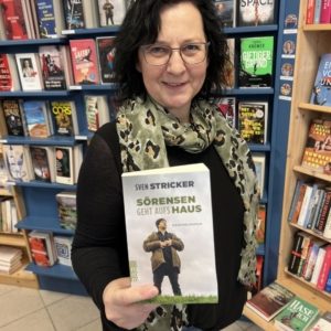 Unsere Buchhändlerin hält das Buch "Sörensen geht aufs Haus" von Sven Stricker in der Hand, zu dem sie eine Rezension geschrieben hat.