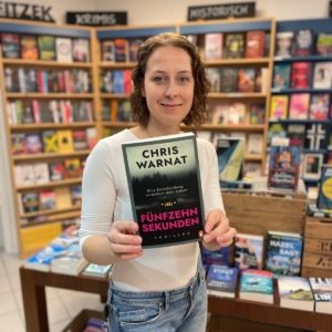 Unsere Buchhändlerin hält das Buch "15 Sekunden" von Chris Warnat in der Hand, zu dem sie eine Rezension geschrieben hat.