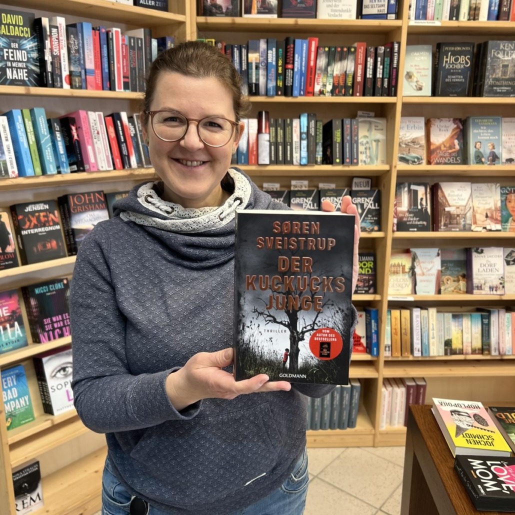Unsere Buchhändlerin hält das Buch "Der Kuckucksjunge" von Soren Sveistrup in der Hand, zu dem sie eine Rezension geschrieben hat.