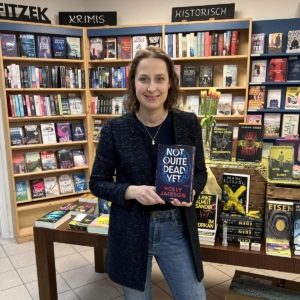 Unsere Buchhändlerin hält das Buch "Not quite dead yet" von Holly Jackson in der Hand, zu dem sie eine Rezension geschrieben hat.