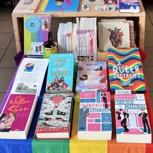 Titelbild für einen Newsbeitrag zu verschiedenen Aktionen anlässlich des Pride Month in den Bücherträumen in Mülheim. Zu sehen ist ein dekorierter Tisch mit queeren Büchern.