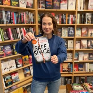 Unsere Buchhändlerin hält das Buch "Safe Space" von Sarah Bestgen in der Hand, zu dem sie eine Rezension geschrieben hat.